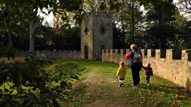 An adult and two small children walk by battlement walls